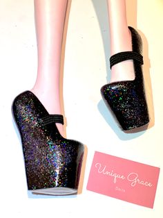 a pair of black glitter high heels on top of a white table next to a pink business card