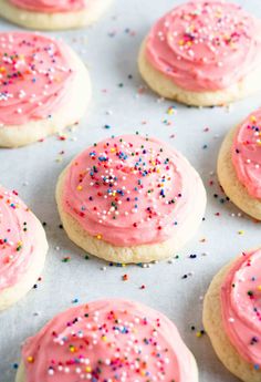 pink frosted cookies with sprinkles on a baking sheet