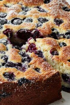 a cake with blueberries and powdered sugar is cut from the plate to be served