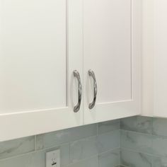 two metal handles on white cabinet doors in a kitchen with marble backsplashes