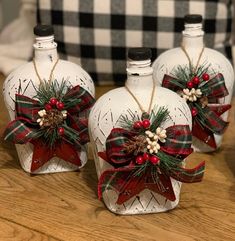 three glass bottles decorated with bows and pine cones on a table next to a plaid pillow