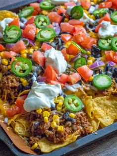 a pizza topped with lots of toppings sitting on top of a pan covered in tortilla chips