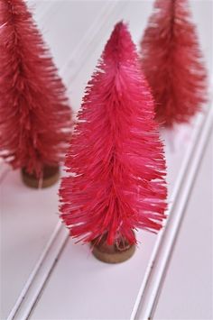 three red christmas trees are sitting next to each other on a white surface with sticks sticking out of them