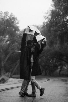 a man and woman walking down the street in the rain with an umbrella over their heads