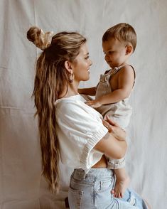 a woman holding a baby in her arms while sitting on top of a wooden stool