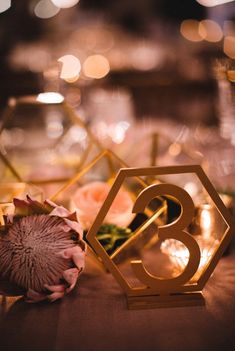 an image of a table number with flowers and candles in the background text reads, geometric table numbers for wedding centerpieces