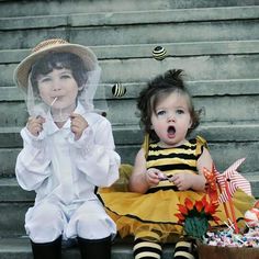 two children dressed in costumes sitting on the steps and one holding up a paper cutout