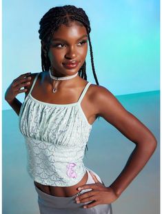 a woman with braids standing in front of a blue background wearing a white top