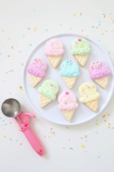 ice cream cones are on a white plate with pink utensils and sprinkles