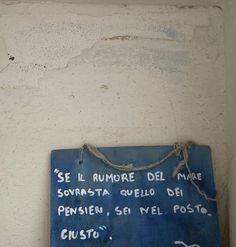 a blue sign hanging on the side of a white wall with writing written in spanish