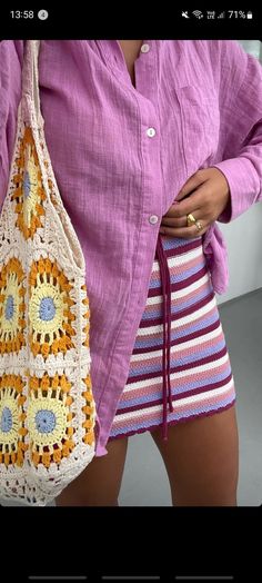 a woman is holding a crocheted bag in her right hand and wearing a purple shirt