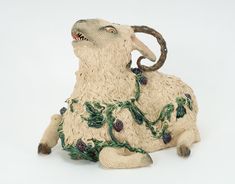 a ceramic sheep with green leaves and berries on it's body, sitting in front of a white background