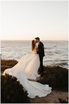 a bride and groom kissing in front of the ocean