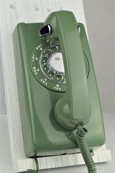 an old fashioned green phone is sitting on a white stand with a cord attached to it