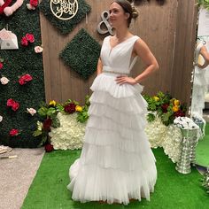 a woman standing in front of a flower display wearing a white dress with tiered layers