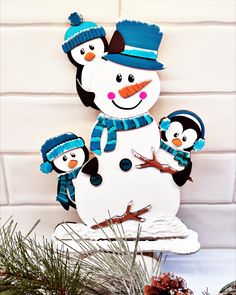 a paper snowman with two penguins on it's head and one penguin is wearing a blue hat