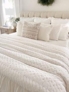 a bed with white sheets and pillows in a bedroom next to a wreath on the wall