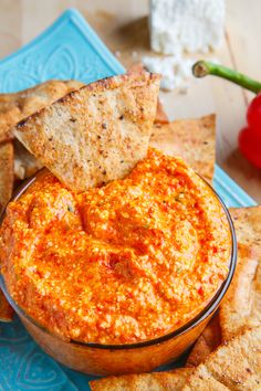 a bowl of dip with tortilla chips and tomatoes in the background on a blue plate