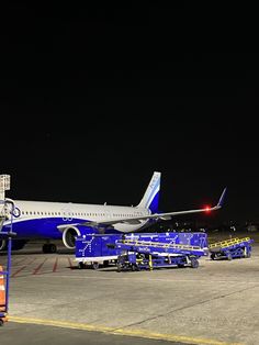 an airplane is parked on the tarmac at night, with luggage carts around it