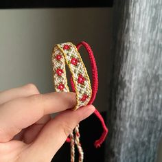 a hand holding two bracelets with red and white beads on them, in front of a window