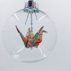 a glass ornament hanging from a chain with an origami bird in it