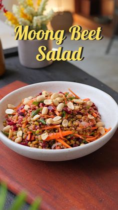 a white bowl filled with carrots and beans on top of a wooden table next to a potted plant