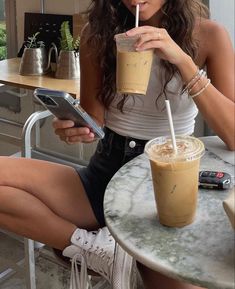 a woman sitting at a table with a drink in her hand and a cell phone