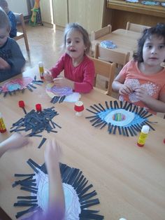 children are sitting at a table making paper sunbursts with glue on them