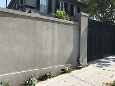 a grey building with black shutters next to a sidewalk