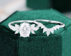 two white gold rings with flowers on them sitting on top of a green velvet box