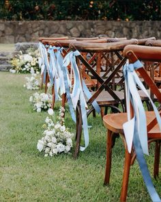 rows of wooden chairs with blue ribbons and flowers on the grass at an outdoor ceremony