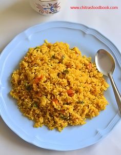 a white plate topped with rice next to a cup and spoon on a tablecloth