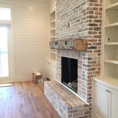 an empty living room with a brick fireplace and built - in shelving units on either side