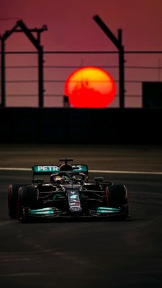 a racing car driving on a track with the sun setting in the distance behind it