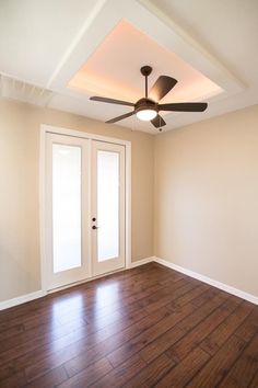 an empty room with a ceiling fan and wooden floors in front of a door that leads to another room