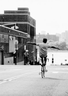 a man riding a bike down a street next to a tall building with a river in the background