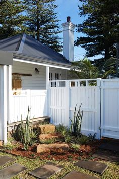 a small white house with a tall chimney in the back yard and stone steps leading up to it