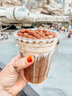 a person holding up a drink in front of a star wars scene at disney world