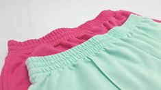 two pairs of pink and green shorts on a white surface, with one showing the bottom part of the pants