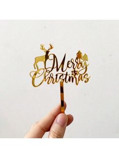 a hand holding up a gold merry christmas cake topper with reindeers on it