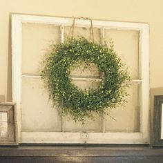 an old window is decorated with a wreath and two small boxes on the mantel