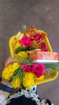 a person holding a basket full of flowers and an orange box with some candy in it