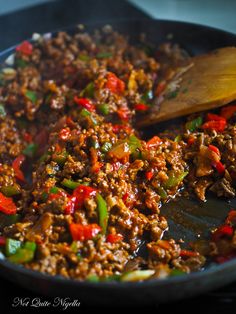 a skillet filled with meat and vegetables on top of a table next to a wooden spoon