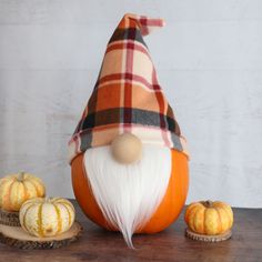 an orange and white gnome sitting on top of a wooden table next to pumpkins