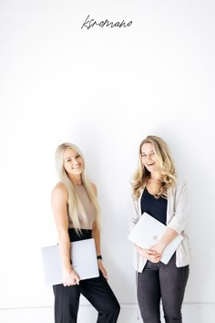 two women standing next to each other with laptops in their hands and one holding a folder