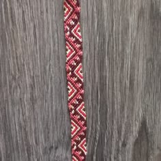 a red and white beaded tie sitting on top of a wooden table next to a piece of wood