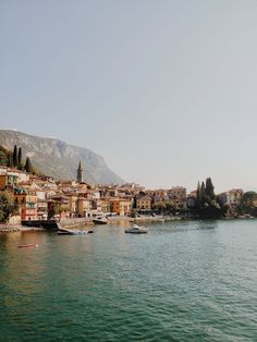 boats are parked on the water in front of some buildings and mountains with trees around them