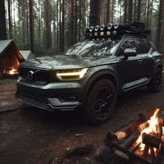 an suv parked in the woods next to a campfire with its lights on,