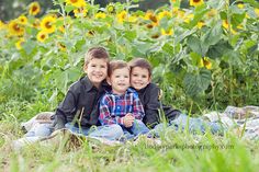 two young boys sitting on a blanket in front of sunflowers with their arms around each other