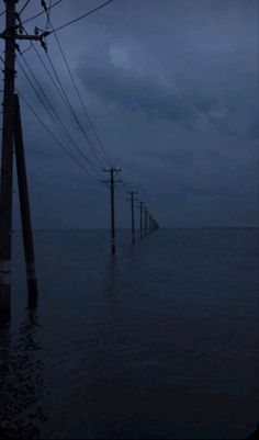 power lines and telephone poles are submerged in the ocean at night, with dark clouds overhead